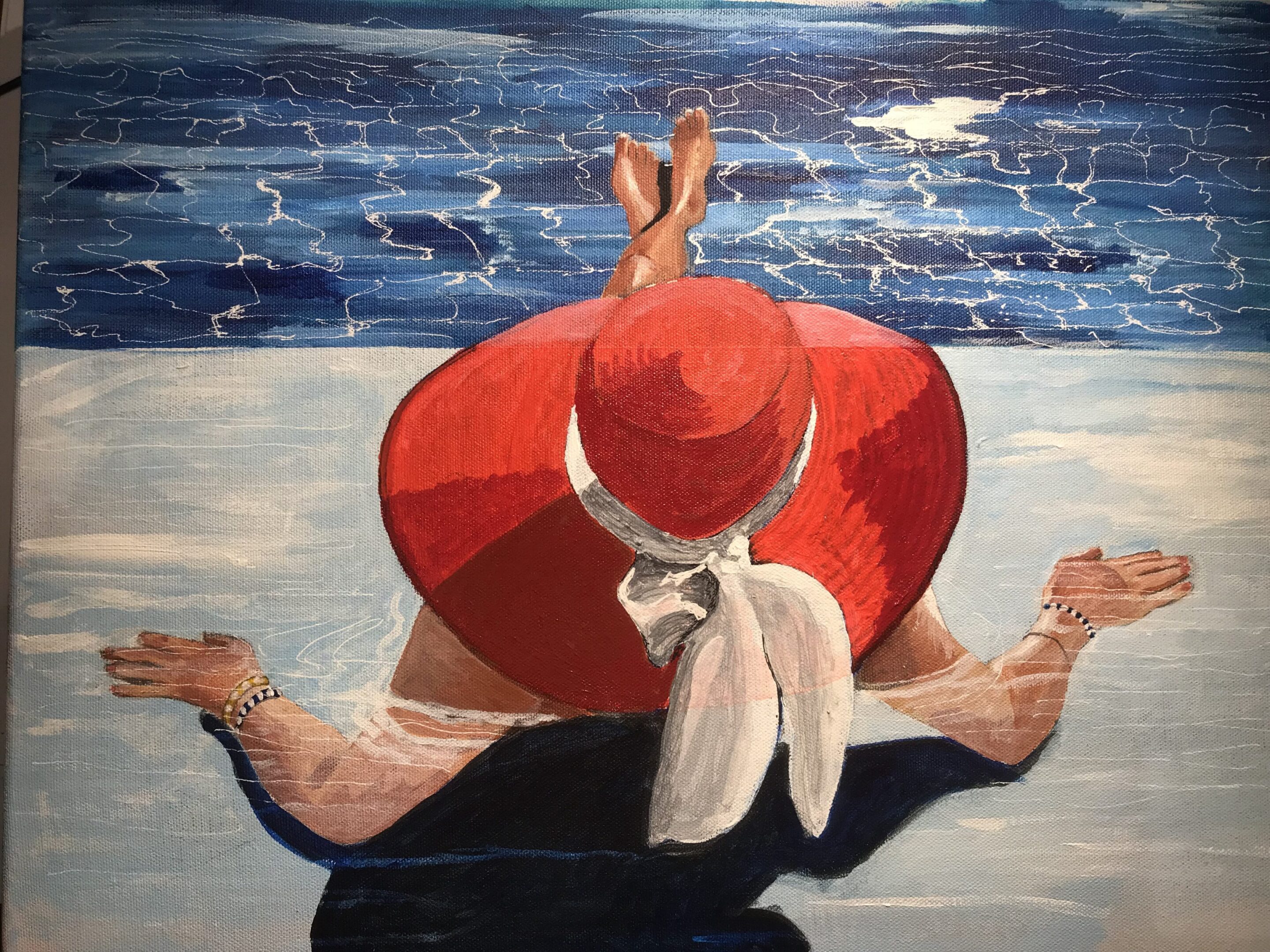 A person in a red hat sitting by the water with legs spread wide.