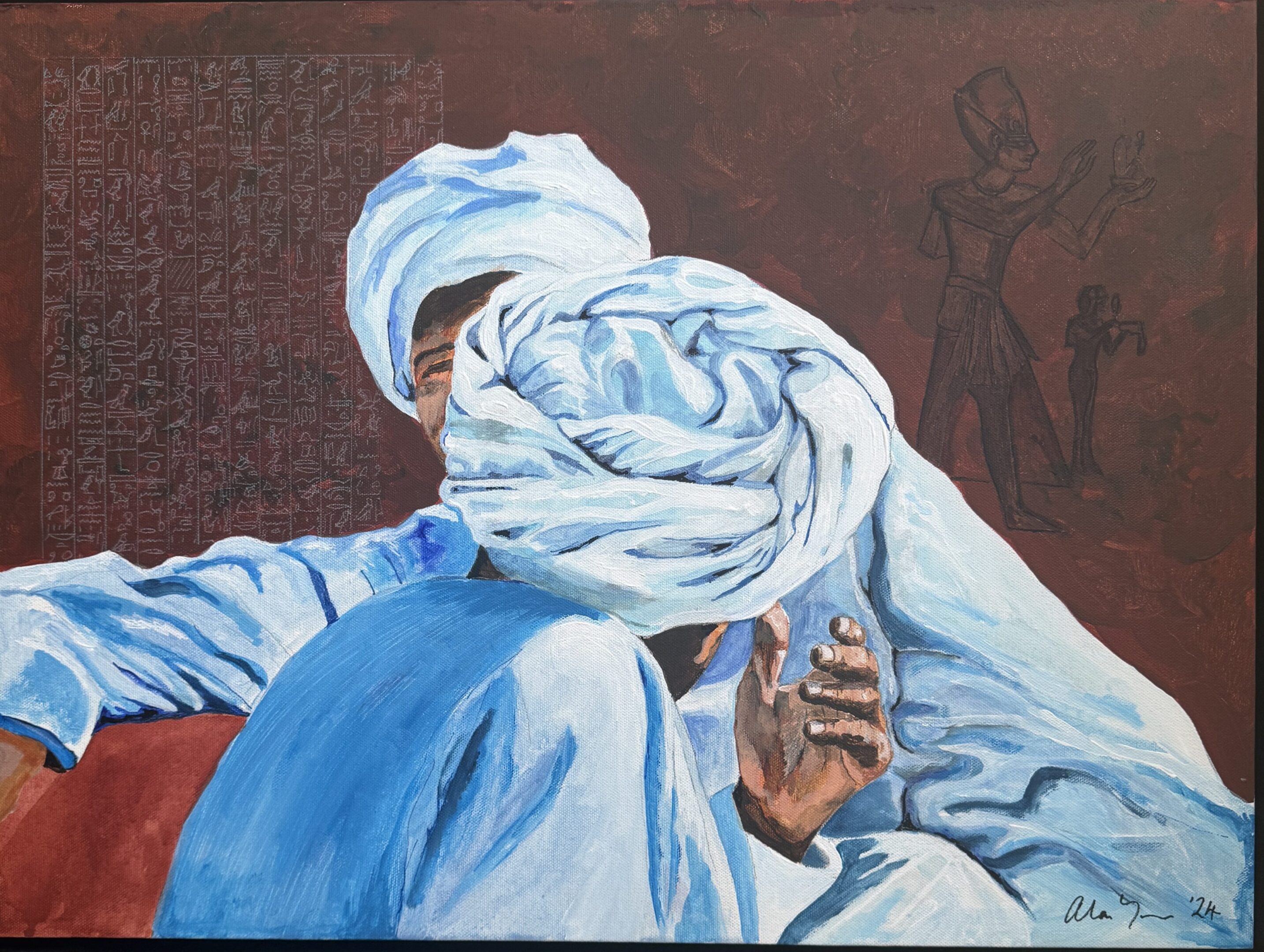 Man in traditional blue attire and white turban sitting thoughtfully.